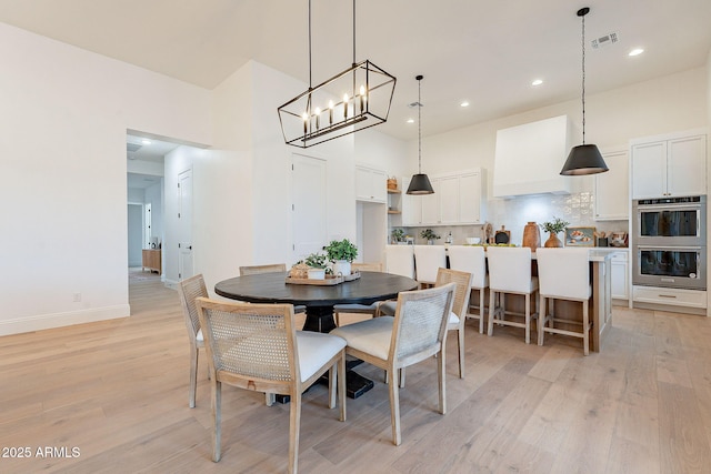 dining area featuring baseboards, visible vents, light wood finished floors, an inviting chandelier, and a high ceiling