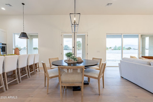 dining area with visible vents, light wood-type flooring, and a high ceiling