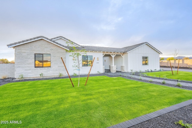 view of front of house with stone siding, fence, a front yard, and a tiled roof