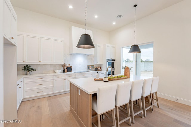 kitchen with a center island with sink, visible vents, white cabinets, black electric stovetop, and tasteful backsplash