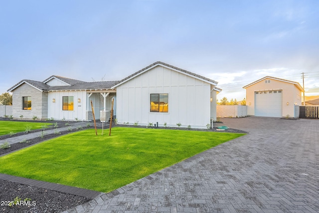 view of front facade with an outbuilding, fence, driveway, a front lawn, and board and batten siding