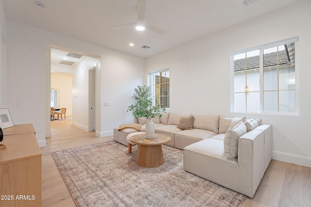 living room featuring ceiling fan, visible vents, baseboards, and light wood-style flooring