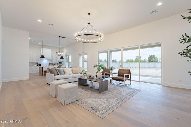 living room featuring baseboards, light wood-style floors, visible vents, and a chandelier