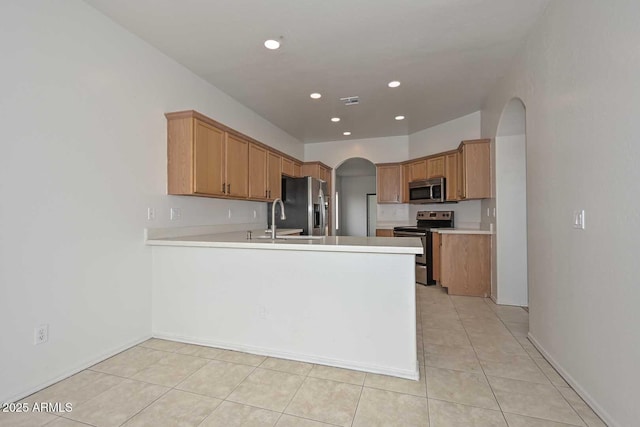 kitchen featuring a sink, arched walkways, appliances with stainless steel finishes, a peninsula, and light countertops