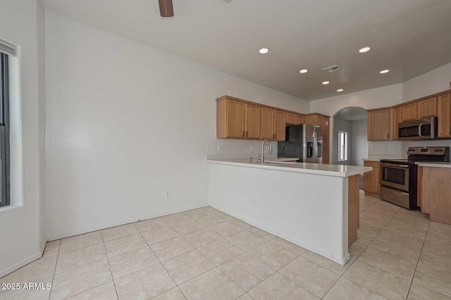 kitchen with arched walkways, a peninsula, appliances with stainless steel finishes, light countertops, and ceiling fan