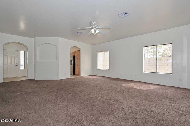 unfurnished living room with visible vents, arched walkways, ceiling fan, and carpet flooring