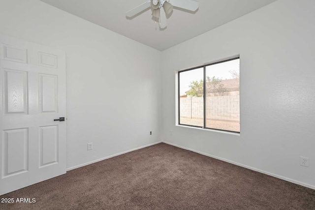 spare room with baseboards, dark colored carpet, and ceiling fan