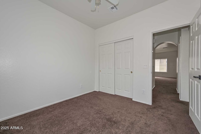 unfurnished bedroom with visible vents, baseboards, a closet, arched walkways, and dark colored carpet