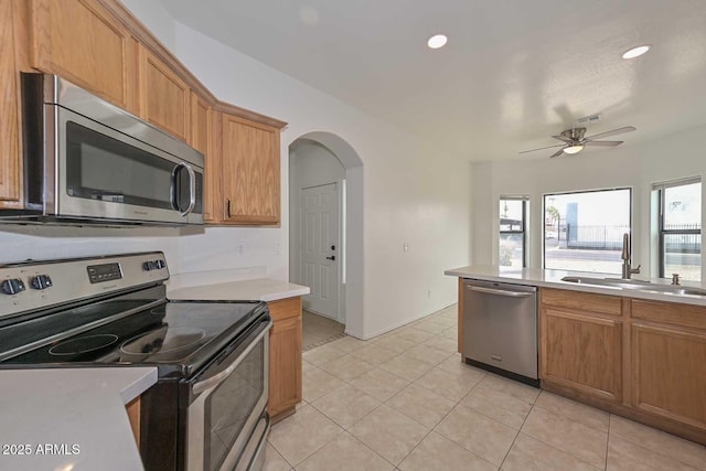 kitchen featuring a sink, arched walkways, appliances with stainless steel finishes, light tile patterned flooring, and light countertops