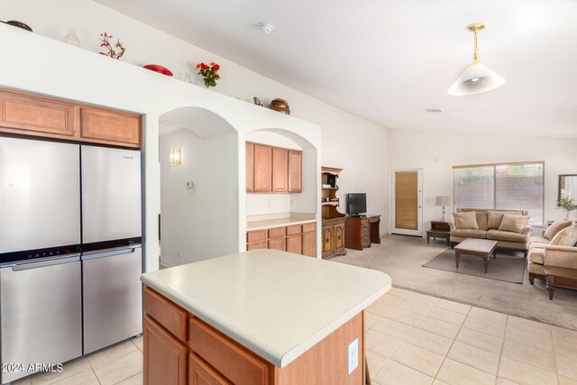 kitchen featuring light colored carpet, pendant lighting, vaulted ceiling, a kitchen island, and stainless steel refrigerator