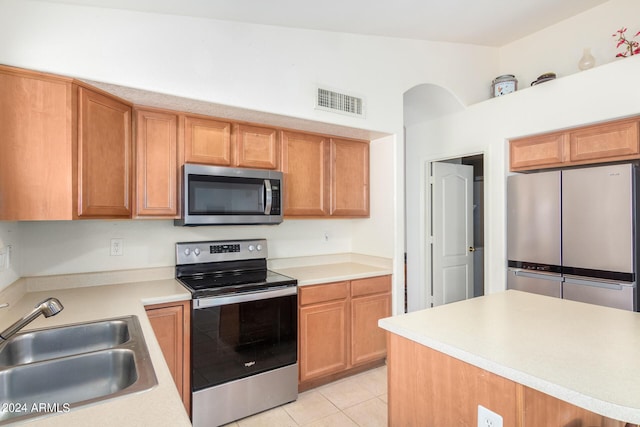 kitchen with stainless steel appliances, light tile patterned flooring, vaulted ceiling, and sink