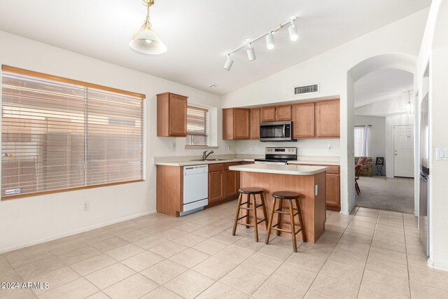 kitchen featuring appliances with stainless steel finishes, track lighting, a center island, light tile patterned floors, and vaulted ceiling