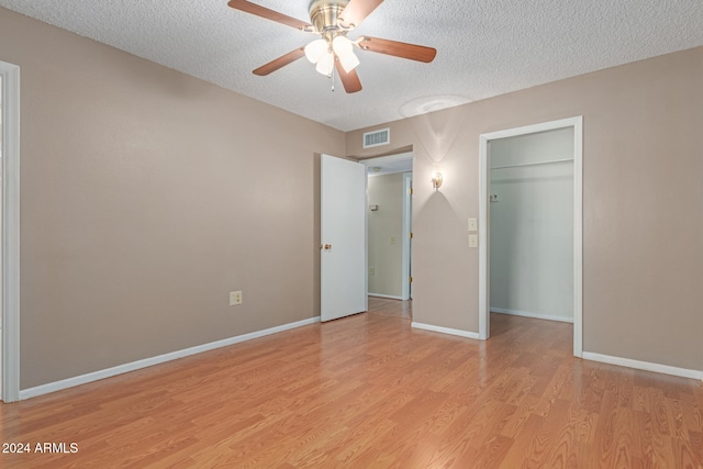 unfurnished bedroom with ceiling fan, light hardwood / wood-style floors, a textured ceiling, a walk in closet, and a closet