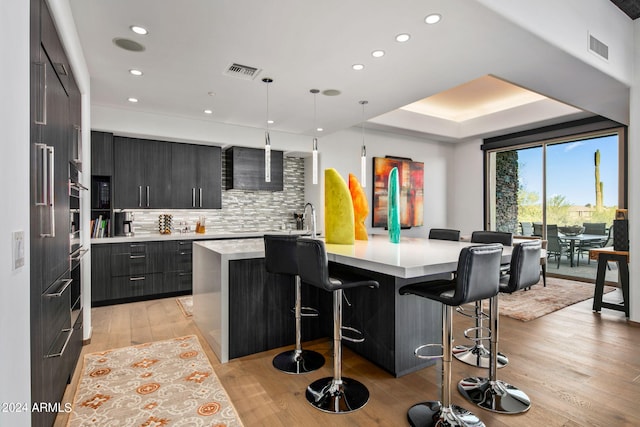 kitchen with an island with sink, hanging light fixtures, light hardwood / wood-style floors, and a breakfast bar