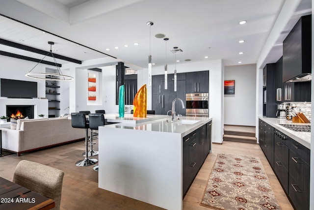 kitchen with light hardwood / wood-style floors, tasteful backsplash, an island with sink, and decorative light fixtures