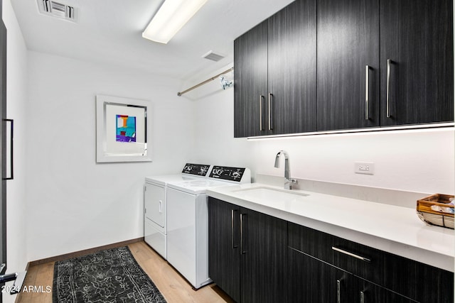 clothes washing area featuring cabinets, sink, light hardwood / wood-style floors, and independent washer and dryer