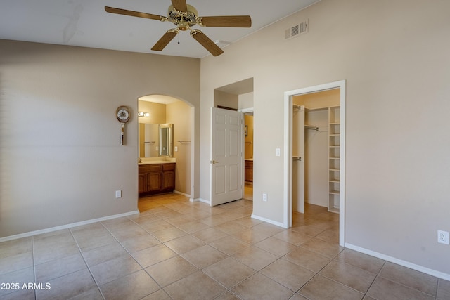 unfurnished bedroom featuring lofted ceiling, ensuite bathroom, a walk in closet, light tile patterned floors, and a closet