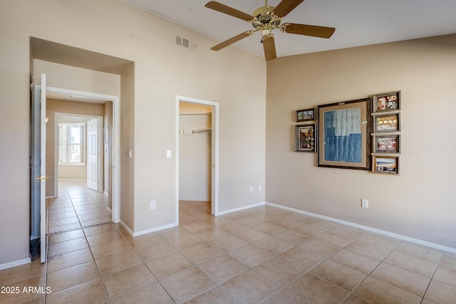 unfurnished bedroom with light tile patterned floors, a spacious closet, a closet, and ceiling fan