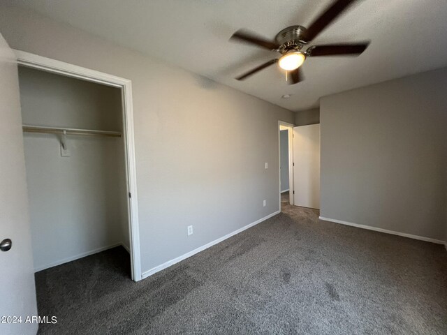 unfurnished bedroom with ceiling fan, dark colored carpet, and a closet