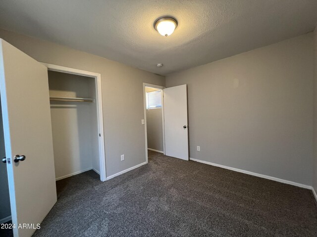 unfurnished bedroom featuring a textured ceiling, dark carpet, and a closet