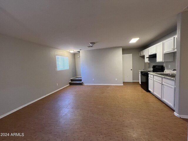 kitchen with light stone countertops, black range, white cabinets, and light hardwood / wood-style floors