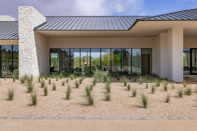 rear view of property with a chimney, a standing seam roof, stucco siding, and metal roof
