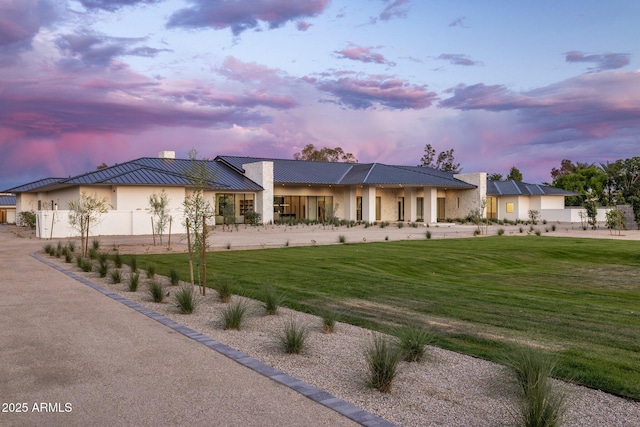 back of house at dusk with a yard, metal roof, stucco siding, and a chimney