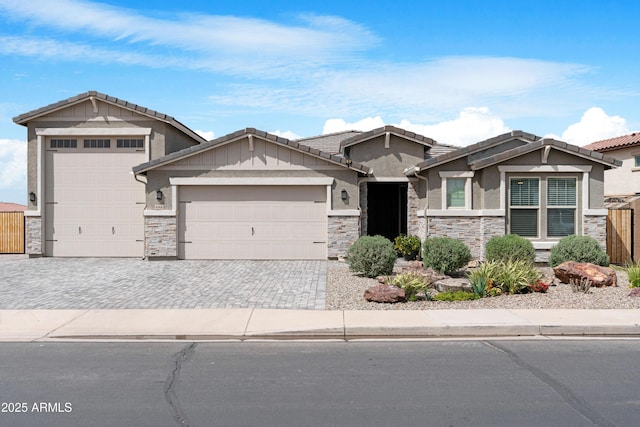 view of front of property featuring stucco siding, fence, an attached garage, stone siding, and driveway