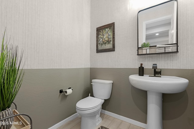 bathroom with toilet, wallpapered walls, baseboards, and wood finished floors