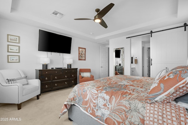 carpeted bedroom with a raised ceiling, a barn door, ensuite bath, visible vents, and ceiling fan