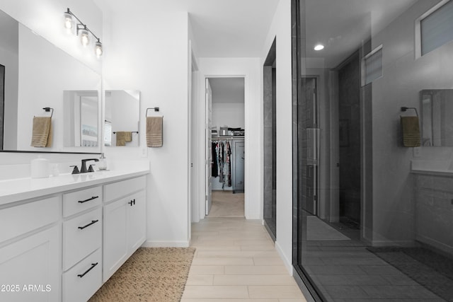 full bath with baseboards, a spacious closet, a tile shower, and vanity