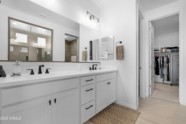 full bath featuring a stall shower, a sink, wood finished floors, a walk in closet, and double vanity