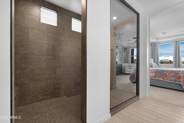 ensuite bathroom featuring connected bathroom, tiled shower, wood finished floors, baseboards, and visible vents