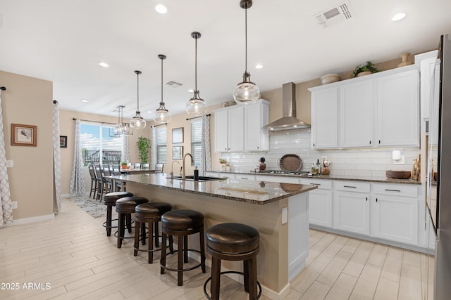 kitchen featuring backsplash, a sink, a breakfast bar, wall chimney range hood, and visible vents