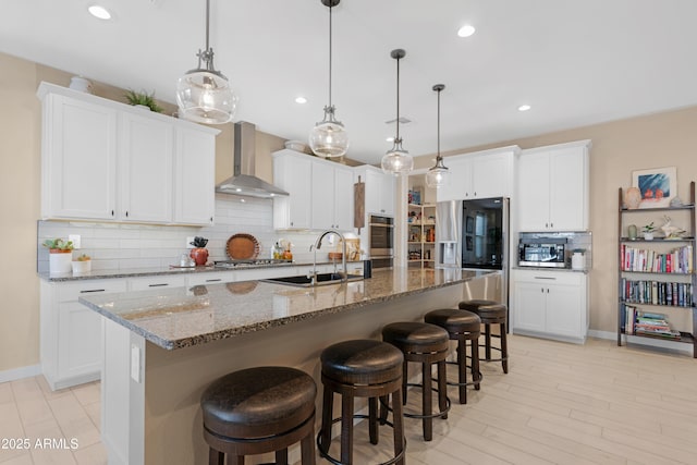 kitchen with a kitchen bar, a sink, white cabinets, appliances with stainless steel finishes, and wall chimney exhaust hood