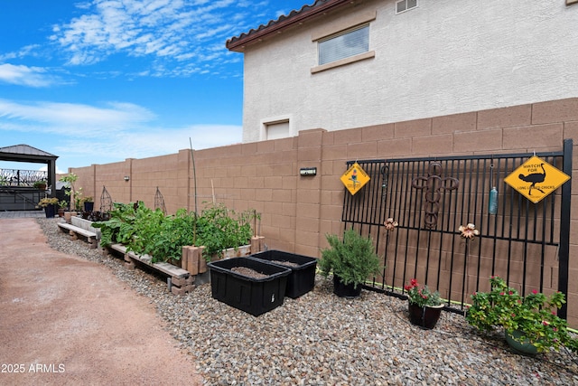 exterior space with a garden, stucco siding, a gazebo, and fence