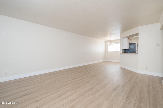 spare room with an inviting chandelier, light hardwood / wood-style floors, and a textured ceiling