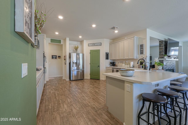 kitchen with a breakfast bar area, wood finished floors, a peninsula, stainless steel fridge with ice dispenser, and light countertops