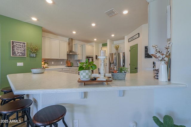 kitchen with visible vents, a peninsula, appliances with stainless steel finishes, wall chimney range hood, and backsplash