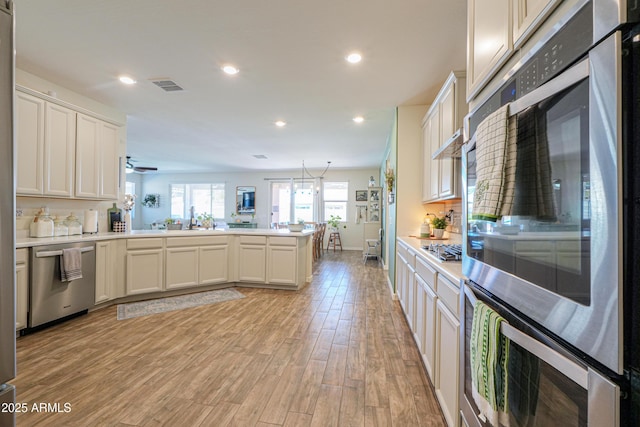 kitchen featuring recessed lighting, light wood-style floors, appliances with stainless steel finishes, a peninsula, and light countertops