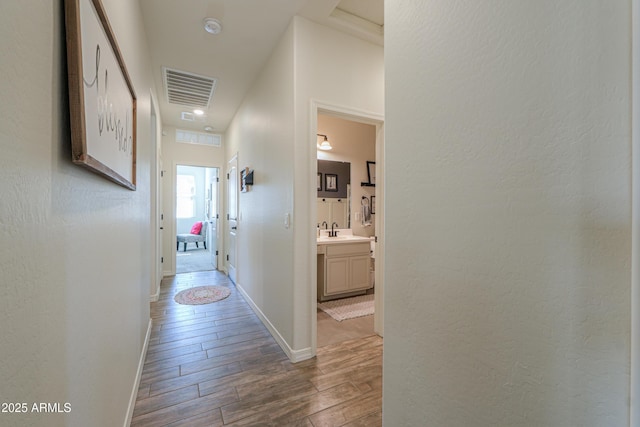 hallway featuring a sink, visible vents, baseboards, and wood finished floors