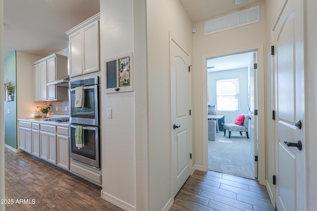 kitchen with gas cooktop, wood finished floors, decorative backsplash, under cabinet range hood, and double oven