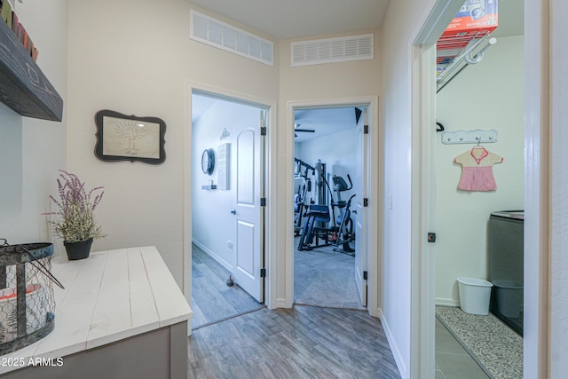 hall featuring visible vents, baseboards, and wood finished floors