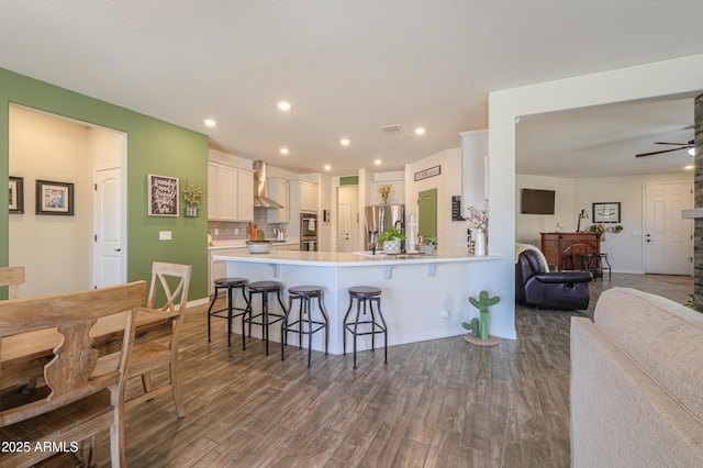 kitchen with stainless steel refrigerator with ice dispenser, a kitchen breakfast bar, wood finished floors, open floor plan, and wall chimney range hood