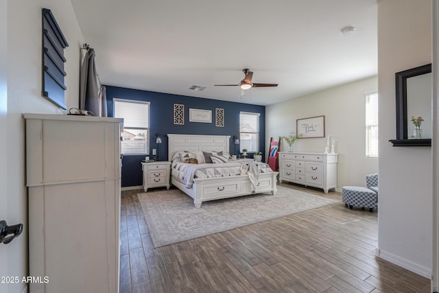 bedroom featuring ceiling fan, visible vents, baseboards, and wood finished floors