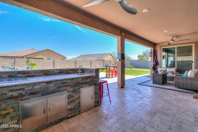 view of patio with an outdoor living space, a fenced backyard, area for grilling, a ceiling fan, and a sink