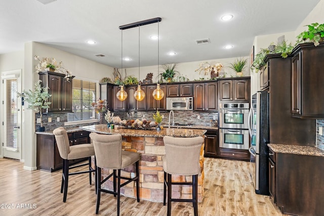 891 W Palo Brea Dr, Litchfield Park, AZ 85340 - kitchen featuring a center island with sink, stainless steel appliances, visible vents, dark brown cabinetry, and pendant lighting