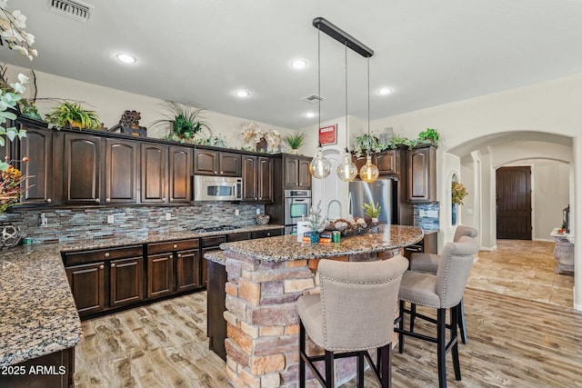 891 W Palo Brea Dr, Litchfield Park, AZ 85340 - kitchen with dark brown cabinets, visible vents, a center island, stainless steel appliances, and a breakfast bar