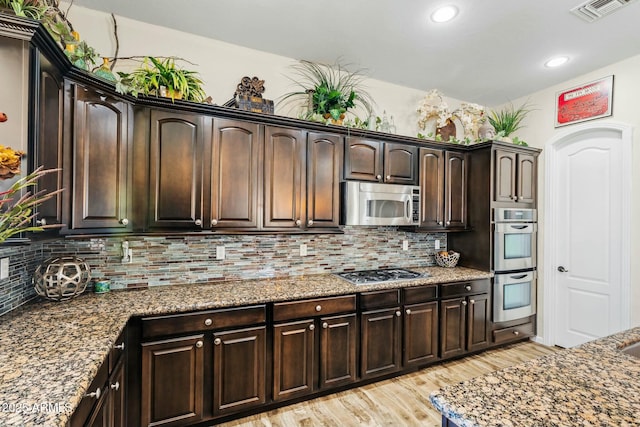 891 W Palo Brea Dr, Litchfield Park, AZ 85340 - kitchen featuring visible vents, dark brown cabinetry, dark stone countertops, light wood-type flooring, and stainless steel appliances