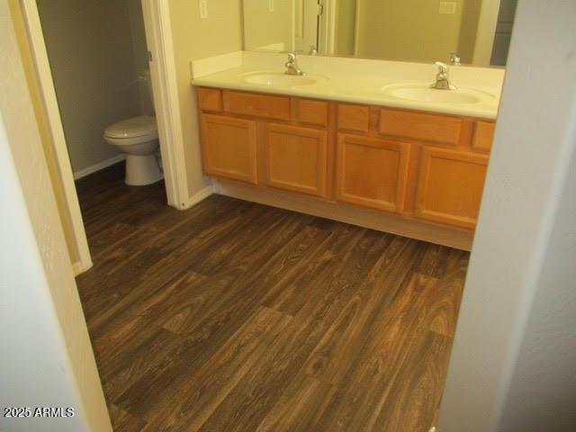 full bath featuring double vanity, wood finished floors, a sink, and toilet